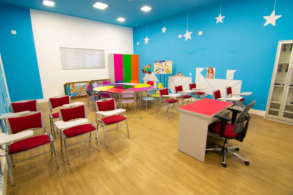 Sala de aula para crianças e jovens com parede azul decorada com estrelas e cadeiras vermelhas