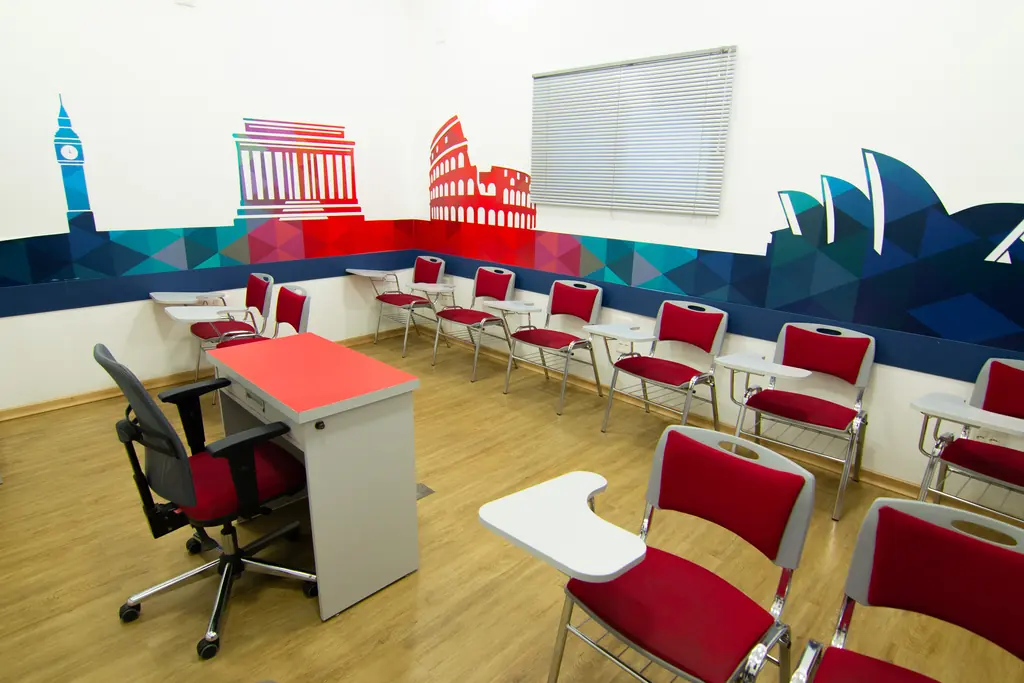 Sala de aula para jovens e adultos com cadeiras vermelhas e mural com monumentos de cidades do mundo